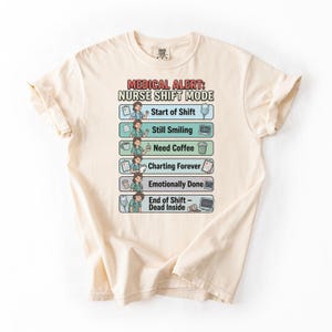 Può includere: T-shirt color crema con la scritta "MEDICAL ALERT: NURSE SHIFT MODE" e illustrazioni delle fasi del turno di un'infermiera. Le fasi includono "Start of Shift", "Still Smiling", "Need Coffee", "Charting Forever", "Emotionally Done" e "End of Shift - Dead Inside."