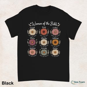 May include: Black t-shirt featuring a floral design with the text "Women of the Bible." Each flower represents a woman from the Bible, with names like Sarah, Ruth, and Esther. The shirt also includes phrases like "Faith like Sarah" and "Love like Naomi."