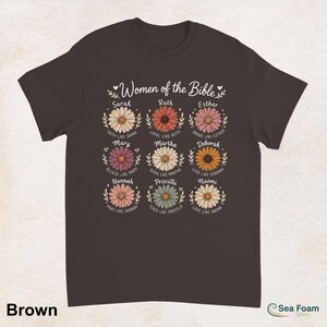 May include: A brown t-shirt featuring the text "Women of the Bible" above nine daisy illustrations, each with a woman's name and a related phrase. The shirt's color is brown.