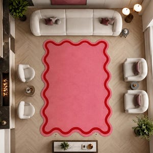 Könnte beinhalten: Ein rechteckiger Teppich mit gewelltem, bogenförmigem Rand. Der Teppich hat eine einfarbige rosa Mitte, die von einem dicken, dunkelroten Wellenrand umgeben ist. Das Design ist symmetrisch, wobei sich das Wellenmuster an allen vier Seiten wiederholt.