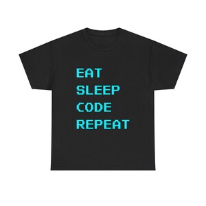 May include: Black t-shirt featuring the text "EAT SLEEP CODE REPEAT" in a pixelated, teal font. The design is centered on the front. The shirt is made of a soft material.