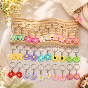 Puede incluir: Una colección de llaveros con forma de flor de colores. Los llaveros presentan varios colores, incluyendo rosa, amarillo, azul y verde. Cada llavero tiene un anillo de metal plateado para sujetar llaves. Las flores tienen pétalos detallados.