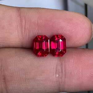 以下が含まれることがあります： エメラルドカットが施された2つの鮮やかな赤色の宝石。長方形の形状と光を反射するファセット面が特徴です。これらのルースストーンは、深く飽和した深紅の色合いを示しており、その透明度を示すために並べて配置されています。