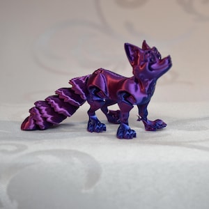 Può includere: Una statuetta di volpe stampata in 3D nei toni del viola e magenta. La volpe ha una coda dettagliata e a strati ed è in posa mentre guarda in alto. La statuetta è su una superficie bianca.