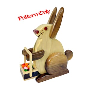 May include: A wooden rabbit toy carrying a basket of colourful sweets. The rabbit is holding a basket with a handle and is painted in brown and light brown wood tones. The rabbit has a red nose and black eyes.