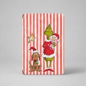 May include: A rectangular tablet case featuring a red and white vertical striped background. The design includes a green creature in a red Santa suit holding a small figure, a brown dog wearing a Santa hat, and a yellow star ornament.