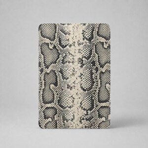 Peut inclure: Un étui de protection rectangulaire pour appareil électronique arborant un motif peau de serpent contrasté. Le design présente une texture d'écailles répétitive dans des tons de noir, gris et blanc cassé, disposée de manière symétrique.