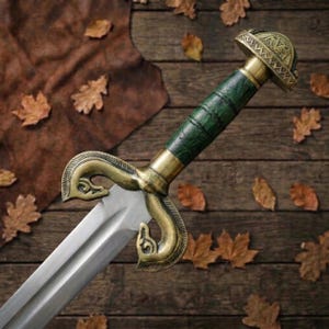 Peut inclure: Une &eacute;p&eacute;e dot&eacute;e d'une lame en acier poli, d'une poign&eacute;e textur&eacute;e vert fonc&eacute; et d'une garde en laiton orn&eacute;e de motifs incurv&eacute;s en forme de t&ecirc;te d'animal. Le pommeau est un capuchon en laiton arrondi avec des gravures complexes.