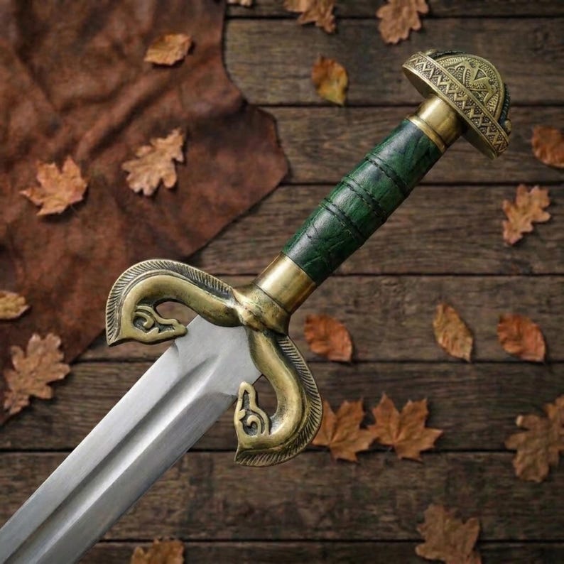 Peut inclure: Une &eacute;p&eacute;e dot&eacute;e d'une lame en acier poli, d'une poign&eacute;e textur&eacute;e vert fonc&eacute; et d'une garde en laiton orn&eacute;e de motifs incurv&eacute;s en forme de t&ecirc;te d'animal. Le pommeau est un capuchon en laiton arrondi avec des gravures complexes.