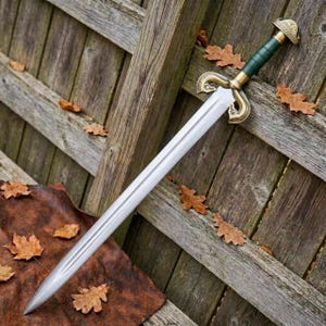 Peut inclure: Une &eacute;p&eacute;e en acier &agrave; double tranchant dot&eacute;e d'une longue lame effil&eacute;e avec une goutti&egrave;re centrale. La poign&eacute;e comprend une prise vert fonc&eacute;, un pommeau en laiton et une garde avec des quillons en laiton courb&eacute;s et orn&eacute;s.