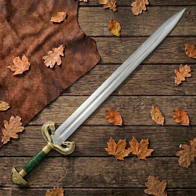 Peut inclure: Une &eacute;p&eacute;e en acier &agrave; double tranchant dot&eacute;e d'une lame pointue, d'une poign&eacute;e textur&eacute;e verte et d'une garde en laiton avec des extr&eacute;mit&eacute;s en forme de t&ecirc;tes d'animaux stylis&eacute;es. L'&eacute;p&eacute;e est plac&eacute;e en diagonale, r&eacute;v&eacute;lant sa finition m&eacute;tallique.