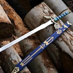 Peut inclure: Une &eacute;p&eacute;e en m&eacute;tal argent&eacute; avec une poign&eacute;e envelopp&eacute;e de bleu et de bleu clair, dot&eacute;e d'une garde dor&eacute;e avec des extensions en forme d'ailes. &Agrave; c&ocirc;t&eacute; se trouve un fourreau bleu d&eacute;cor&eacute; de symboles g&eacute;om&eacute;triques dor&eacute;s et d'une pointe dor&eacute;e.