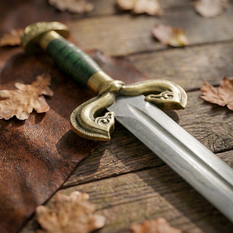 Peut inclure: Une &eacute;p&eacute;e dot&eacute;e d'une lame en acier &agrave; double tranchant, d'une garde en laiton orn&eacute;e de volutes et d'une poign&eacute;e vert fonc&eacute;. Le pommeau est en laiton et l'arme est positionn&eacute;e en diagonale dans le cadre, mettant en valeur sa finition m&eacute;tallique.