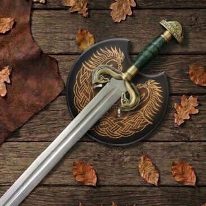 Peut inclure: Une &eacute;p&eacute;e en acier avec une poign&eacute;e verte et une garde en laiton orn&eacute;e de motifs de t&ecirc;tes d'animaux. L'&eacute;p&eacute;e repose sur un bouclier noir circulaire d&eacute;cor&eacute; d'un motif de n&oelig;uds celtiques dor&eacute; repr&eacute;sentant un cheval, sur une surface en bois.
