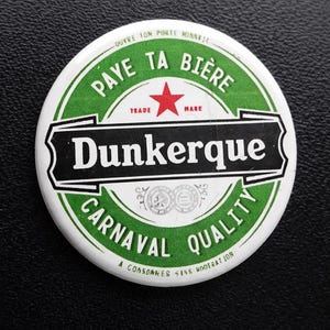 Peut inclure: Un badge rond avec un design vert et blanc et une étoile rouge. Le texte indique PAYE TA BIÈRE, Dunkerque, CARNAVAL QUALITY, OUVRE TON PORTE MONNAIE et A CONSOMMER SANS MODERATION, avec deux petits emblèmes circulaires au centre du badge.