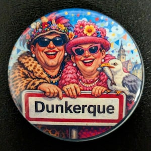 Peut inclure: Un badge rond illustrant deux personnes souriantes portant des chapeaux à fleurs, des lunettes de soleil et des colliers, appuyées sur un panneau blanc à bordure rouge portant l'inscription Dunkerque, avec un goéland tenant un poisson.