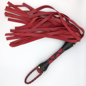 Puede incluir: Un l&aacute;tigo de cuero rojo con un mango trenzado negro y detalles dorados.