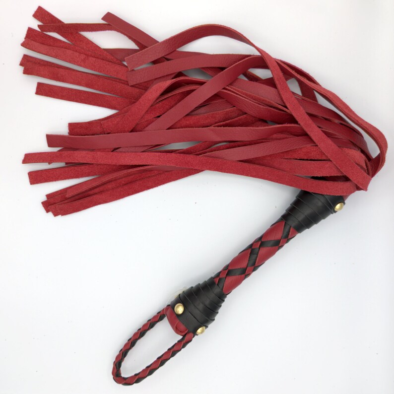 Puede incluir: Un l&aacute;tigo de cuero rojo con un mango trenzado negro y detalles dorados.
