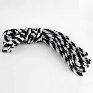 May include: A length of rope with a black, white, and gray chevron pattern. The rope is coiled and tied in the middle. The rope is on a white background.