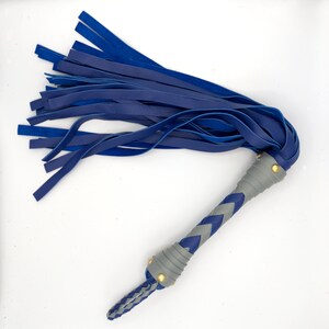 Puede incluir: Un l&aacute;tigo de cuero azul con un mango trenzado y detalles dorados.
