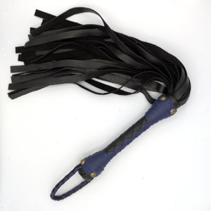 Puede incluir: Un l&aacute;tigo de cuero negro con un mango trenzado azul y detalles en lat&oacute;n.