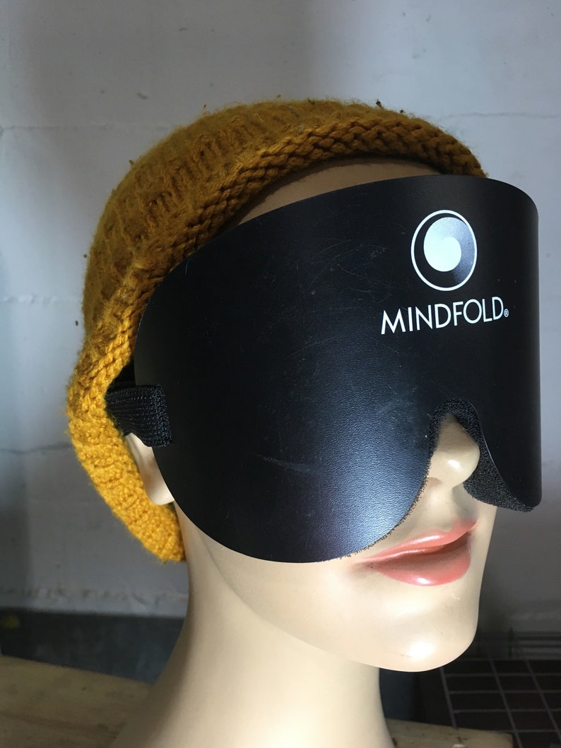 Pu&ograve; includere: Maschera per dormire nera con il testo "MINDFOLD." stampato in bianco. La maschera &egrave; indossata da un manichino con un berretto di lana giallo senape.