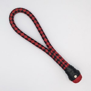 May include: A red and black braided leather whip with a black leather handle and a silver metal accent.