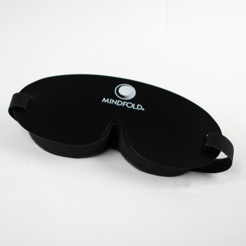 Pu&ograve; includere: Maschera per dormire nera con un logo bianco che dice "MINDFOLD." La maschera ha una forma sagomata e un cinturino regolabile.