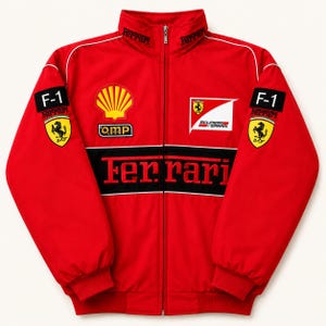 Könnte beinhalten: Eine leuchtend rote Reißverschlussjacke mit einem Stehkragen, auf dem das Wort Ferrari eingestickt ist. Auf der Brust befinden sich ein gelbes Shell-Logo, ein OMP-Aufnäher und das Scuderia Ferrari-Emblem. Ein schwarzer Streifen zeigt Ferrari.