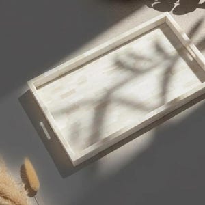 May include: Rectangular serving tray with a light-colored, mosaic-like surface and a raised border. The tray has integrated handles and is made of a light-colored material. The tray is empty and sits on a neutral surface.