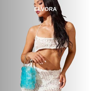 May include: A white lace two-piece outfit, comprising a crop top and skirt. A light blue, bubble-shaped handbag with a gold chain strap is held. The word "ELVORA" is printed in white at the top of the image.