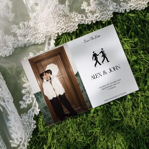 May include: A rectangular Save the Date card featuring a photograph of two people in white jackets and black trousers kissing in front of a wooden door. The card includes the text Alex & John, Saturday 28th October 2028, Brooklyn, New York City.