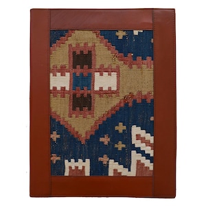 May include: A rectangular leather portfolio featuring a central panel of woven fabric. The brown leather border frames a blue, tan, and red geometric pattern. The textile displays a repeating diamond motif with small cross shapes and white accents.