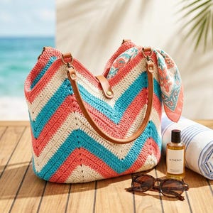 Peut inclure: Nature morte sur le thème de la plage avec un grand sac fourre-tout en crochet à chevrons corail, blanc et turquoise. Le sac a des poignées en cuir marron. Sont également présents des lunettes de soleil, une bouteille d'huile, une serviette rayée roulée et un foulard à motifs.