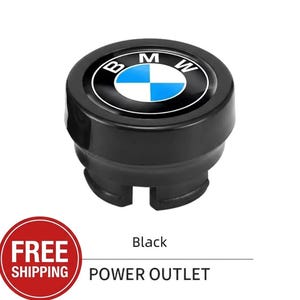May include: Black power outlet cover with the BMW logo. The logo features a white and blue emblem with the letters "BMW" in white. The text "POWER OUTLET" is below the cover.