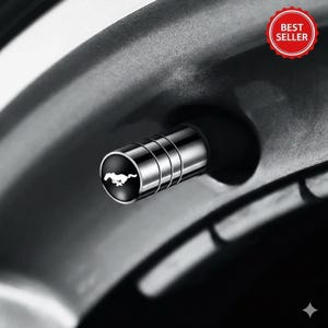 Op de afbeelding: Een close-up van een chromen ventieldopje met een zwart cirkelvormig embleem met een wit rennend paard. De dop heeft drie horizontale groeven, tegen een donkere achtergrond.