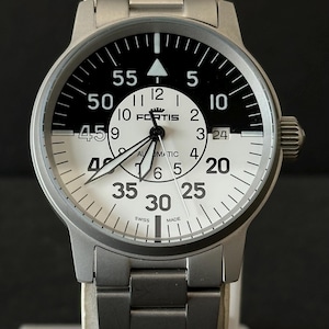 May include: A silver wristwatch with a black and white face. The watch face features the brand name "FORTIS", and the words "SWISS MADE". The watch has a stainless steel strap and a crown on the right side.