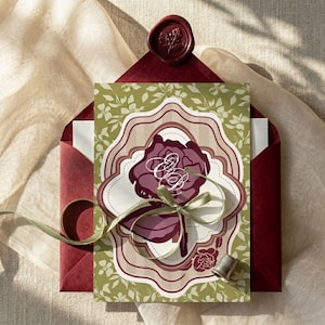 May include: An invitation suite featuring a burgundy rose design with the initials "E & D" on a decorative card. The card is inside a burgundy envelope, sealed with a wax stamp. A green ribbon and thimble are also present.
