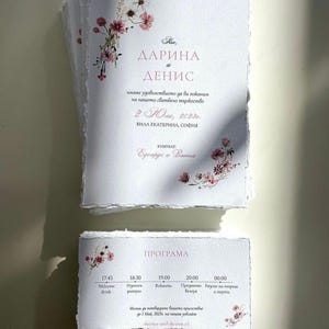 Peut inclure: Ensemble de faire-part de mariage sur papier texturé avec bords dentelés. Les cartes sont ornées de motifs floraux roses et blancs et de texte rose clair. L'invitation comprend les noms "ДAРИНА et ДЕНИС".