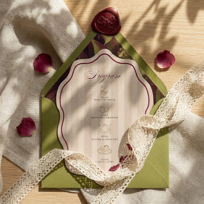 May include: A wedding program card inside a green envelope, sealed with a red wax stamp. The card has a cream background with vertical stripes and the word "Program" at the top. A cream lace ribbon and scattered rose petals complete the elegant design.