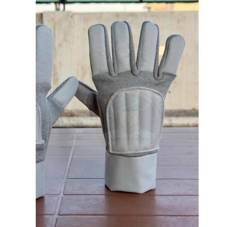 May include: A pair of gray work gloves with white leather palms and padded knuckles. The gloves have a gray fabric cuff and are designed for protection and durability. The gloves are shown on a brown surface.