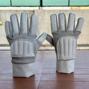 May include: A pair of gray work gloves with padded knuckles and wrist cuffs. The gloves are made of a combination of materials, with a light gray fabric on the palms and fingers and a darker gray fabric on the back of the hand and wrist.