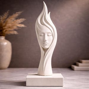 May include: A white sculpture depicting a face with closed eyes, surrounded by flowing, flame-like shapes. The sculpture sits on a rectangular base. The artwork creates a sense of peace, suitable for home decor, and is made of an unknown material.