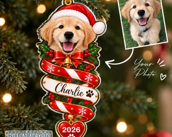 May include: A flat acrylic Christmas ornament featuring a golden retriever puppy wearing a Santa hat, a red bow with a gold bell, a white ribbon banner with the name Charlie and a paw print, and a heart-shaped tag displaying the year 2026.