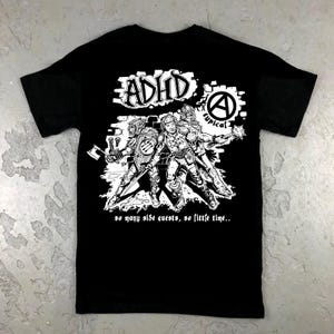 May include: Black t-shirt with a white graphic. The design includes the word "ADHD" and a drawing of three figures in armour. The text "so many side quests, so little time..." is below.