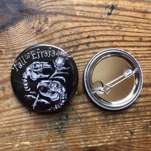 Puede incluir: Un botón blanco y negro con un diseño de calavera y cardo. El texto "Fall of Efrafa" está impreso en el botón.