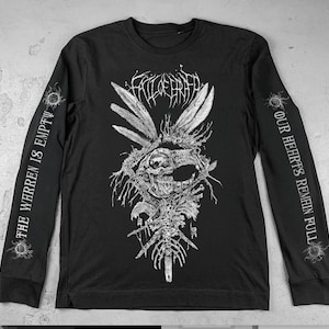Puede incluir: Camiseta negra de manga larga con un detallado gráfico blanco en la parte delantera que representa una calavera, plumas y huesos. Las mangas tienen el texto "THE WARREN IS EMPTY" y "OUR HEARTS REMAIN FULL".