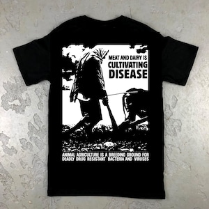 May include: Black t-shirt with a white graphic. The graphic shows a person working in a field with a cow, and the text "MEAT AND DAIRY IS CULTIVATING DISEASE." Below, it reads "ANIMAL AGRICULTURE IS A BREEDING GROUND FOR DEADLY DRUG RESISTANT BACTERIA AND VIRUSES."