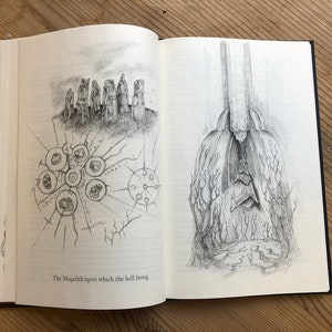 May include: Open book with two detailed pencil illustrations. One depicts a stone structure with a circular diagram. The other shows a tall, draped figure with a textured base. The text at the bottom reads: "The Megalith upon which the bell hung."