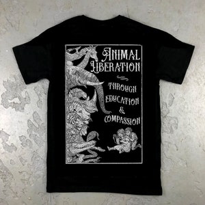 May include: Black t-shirt with a white graphic print of animals stacked on top of each other. The text "Animal Liberation Through Education & Compassion" is printed on the graphic.